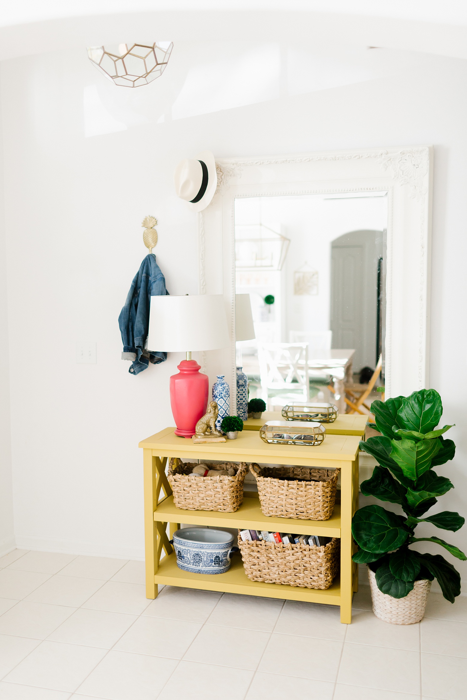 A bright, fresh and colorful entryway, yellow shelf, fiddle leaf fig, all white walls, brass light fixture, bright and colorful home